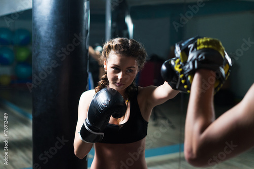 Young fighter boxer fit girl wearing boxing gloves in training with personal trainerin gym. Low key selective focus image. Woman power