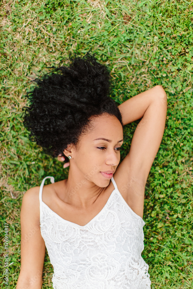 A beautiful woman with curly hair laying down in the grass daydreaming A beautiful woman with curly hair laying down in the grass daydreaming