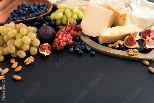 Tasting cheese dish with fruits, berries on old black cheeseboard. Food for wine and romantic, cheese delicatessen. Top view. space for text