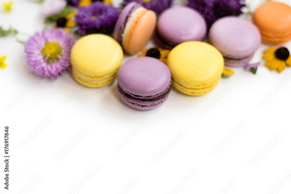 Colorful macarons, flowers and leaves on a white background. Colorful french dessert with fresh flowers. Autumn concept Colorful macarons, flowers and leaves on a white background. Colorful french dessert with fresh flowers. Autumn concept