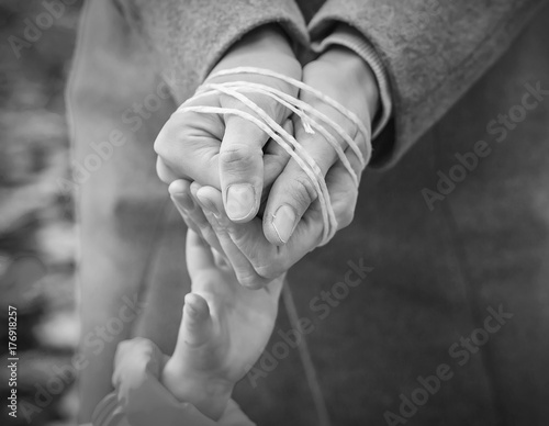 child's hand reaches out to the rope-tied hands of the parent. Black and white image. Woman's hands tied with rope. Violence in family concept.