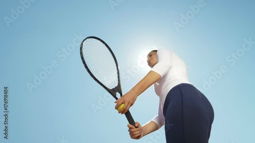 Beautiful young girl tennis player woman serving ball with racket outdoor with sun behind her