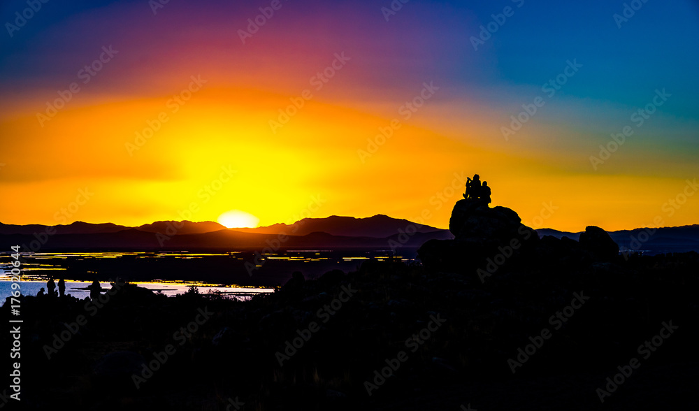 two persons standing on a rock watching a colorful sunset