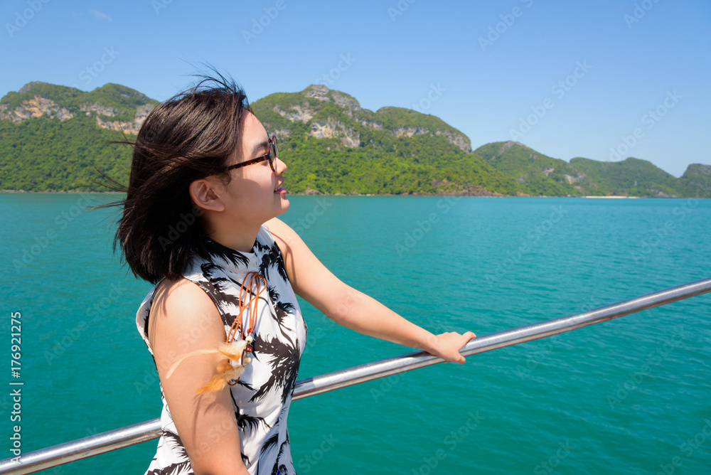 Obraz premium Cute young woman with eyeglasses smiling happily on the boat while cruising the beautiful natural of the blue sea and sky in summer at Mu Ko Ang Thong National Park, Surat Thani, Thailand