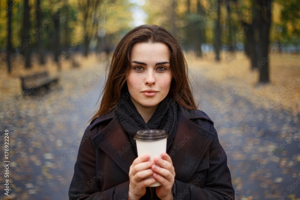 Young woman wearing stylish checkered coat walking in the autumn park and drinking take away coffee in paper cup. Breakfast on the go, warming up, autumn concept Young woman wearing stylish checkered coat walking in the autumn park and drinking take away coffee in paper cup. Breakfast on the go, warming up, autumn concept