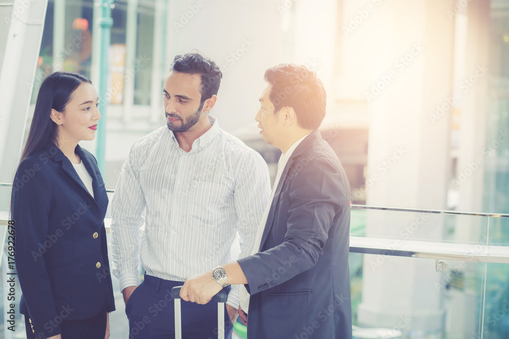 Fototapeta premium Two handsome young businessmen and lady in classic suits are holding cups of coffee, talking and smiling, standing outside the office building.