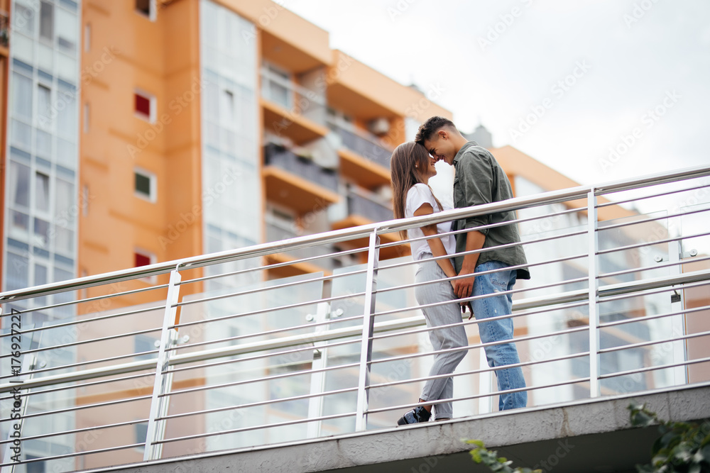 Happy young couple hugging and kissing on bridge in modern city