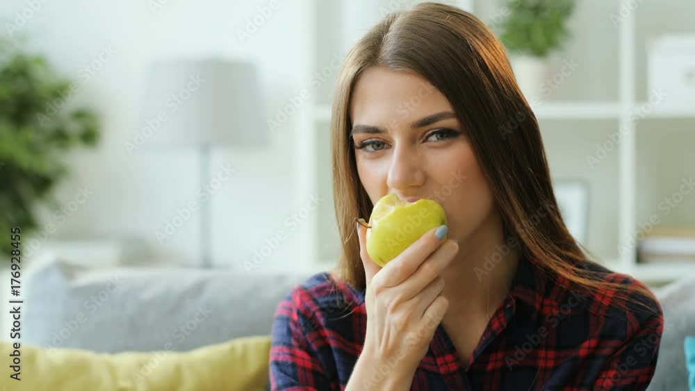 Beatiful brunette woman eating fresh green apple while resting on the sofa at home. Close up shot. Beatiful brunette woman eating fresh green apple while resting on the sofa at home. Close up shot.