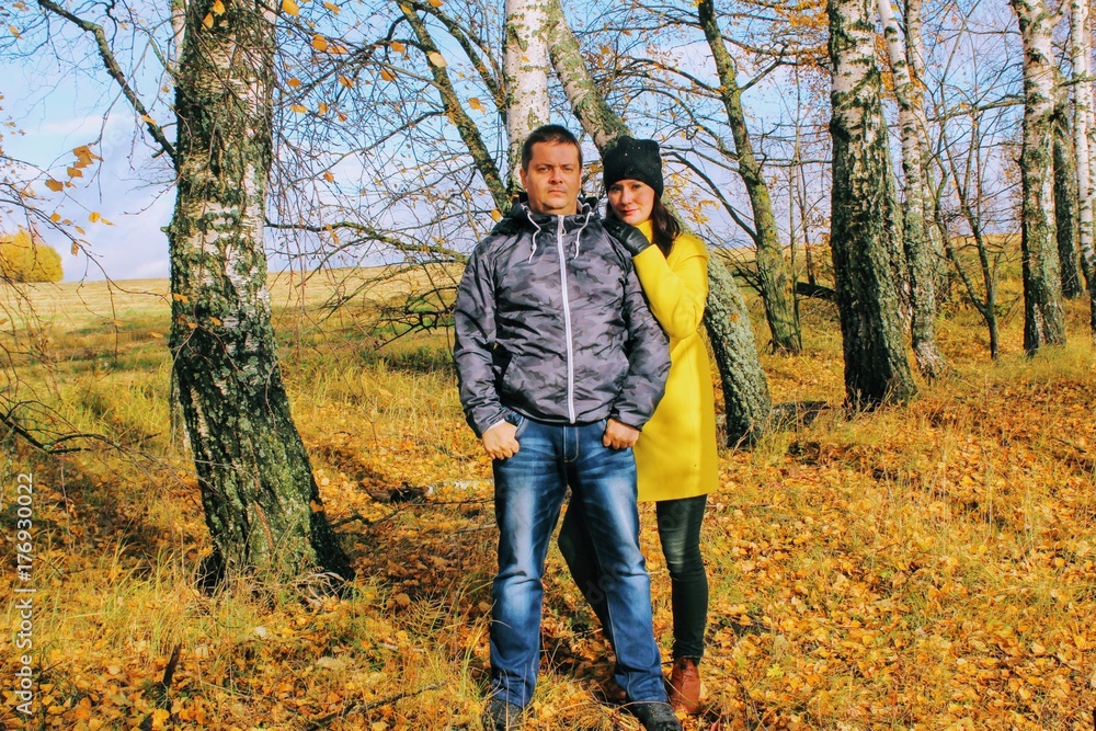 Autumn time: young couple posing against a background of autumn birch forest.
