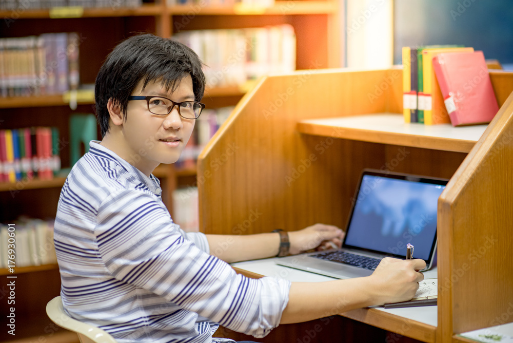 Young Asian man university student thinking about his project homework and using laptop computer in library, education research and self learning in university life concepts Young Asian man university student thinking about his project homework and using laptop computer in library, education research and self learning in university life concepts