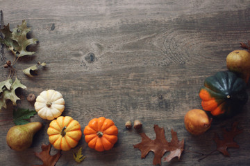Thanksgiving season still life with colorful small pumpkins, acorn squash, fruit and fall leaves over rustic wooden background