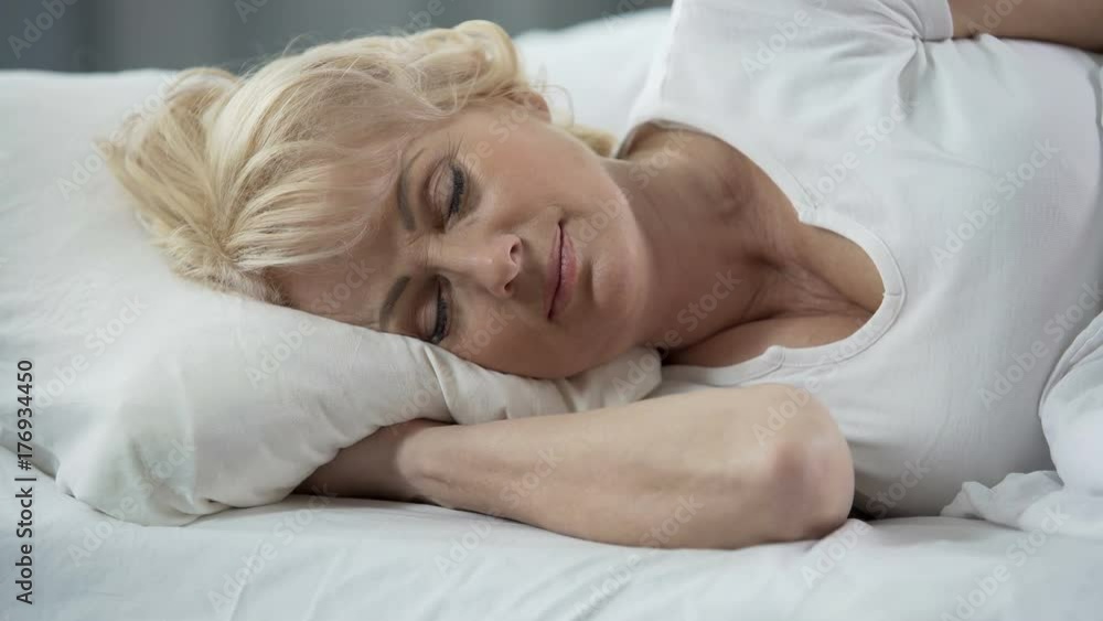 Close-up of beautiful blond mature lady lying in bed, healthy sleep, retirement Close-up of beautiful blond mature lady lying in bed, healthy sleep, retirement