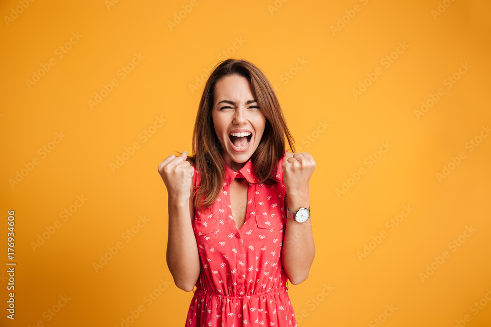Close-up of emotional brunette woman keeping hands in fists, screaming while celebrating win Close-up of emotional brunette woman keeping hands in fists, screaming while celebrating win