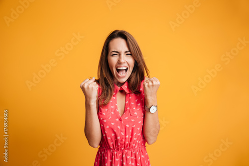 Close-up of emotional brunette woman keeping hands in fists, screaming while celebrating win photo
