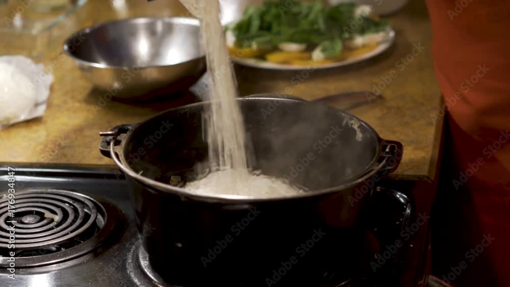 In a large cast iron pot with onions and shiitake mushrooms, a chef takes pours in arborio rice for risotto. In a large cast iron pot with onions and shiitake mushrooms, a chef takes pours in arborio rice for risotto.