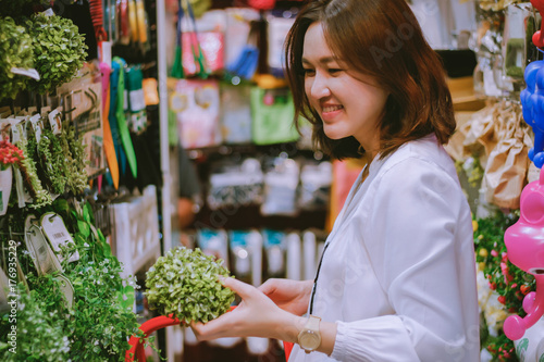 Asian woman deciding to buy artificial green plant for home decoration at retail shop