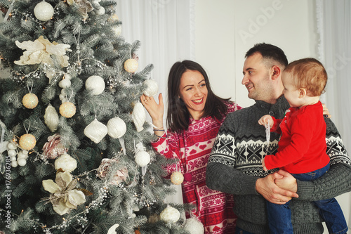 A fun , happy family with Christmas gifts. Parents and little baby having fun near the Christmas tree in the room. Loving family by the Christmas tree