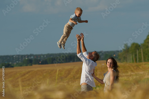 Young parents and kid walking through wheat field