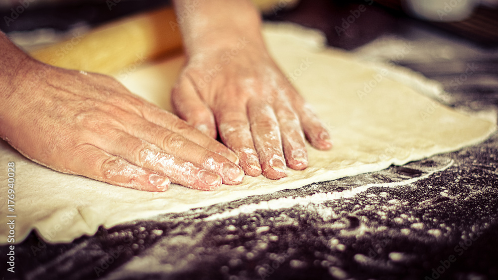 Cooking at home concept: vintage faded image of a woman’s hands preparing dough for a pie on the kitchen table