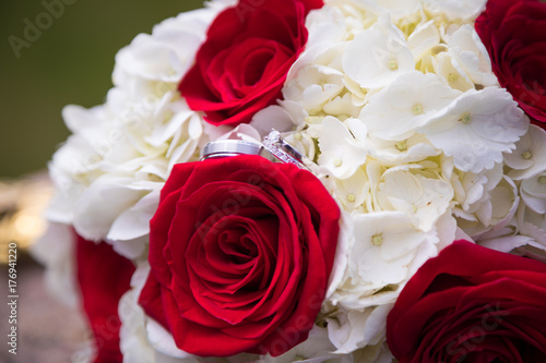 His and hers wedding rings on bridal bouquet of red roses and white hydrangeas. 