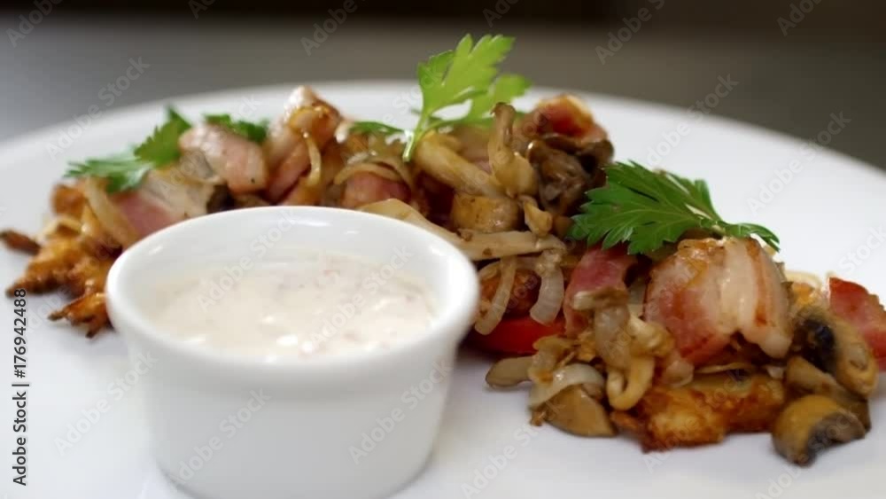 Close up of spinning white plate with delicious potato latkes and topping of ham, onions and mushrooms with garlic sauce for dipping Close up of spinning white plate with delicious potato latkes and topping of ham, onions and mushrooms with garlic sauce for dipping