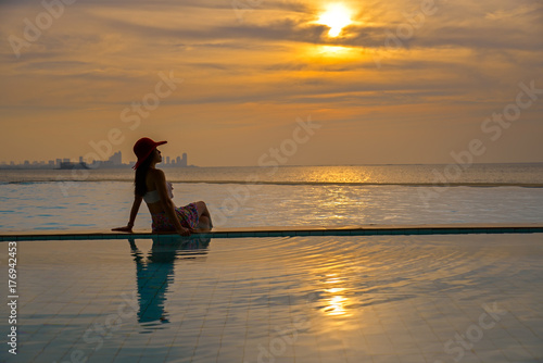 Summer day, asian young woman happy in big hat relaxing on the swimming pool, travel near the sea and beach in the sunset. Summer Concept © freebird7977