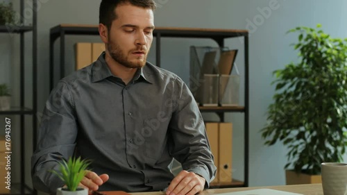 Portrait of tired young businessman opening his diary to checking plans for tommorow while drinking coffe in the office. photo