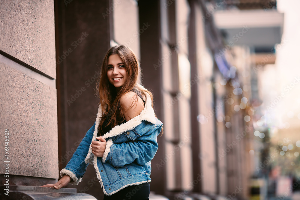 Outdoor portrait of a young beautiful fashionable happy lady posing on a street city. Model wearing stylish clothes. Girl looking up. Female fashion. City lifestyle. Copy space for text