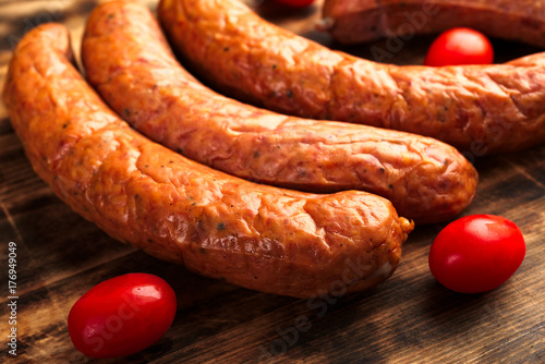 Deliciously smoked handmade Swedish Isterband sausages with natural casing. Here on burnt wooden cutting board with red tomatoes.