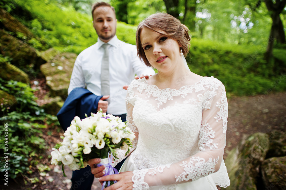Newlyweds posing with huge rocks on the background in the forest on a wedding day. Newlyweds posing with huge rocks on the background in the forest on a wedding day.