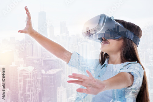Smiling girl in VR headset reaching to the sky