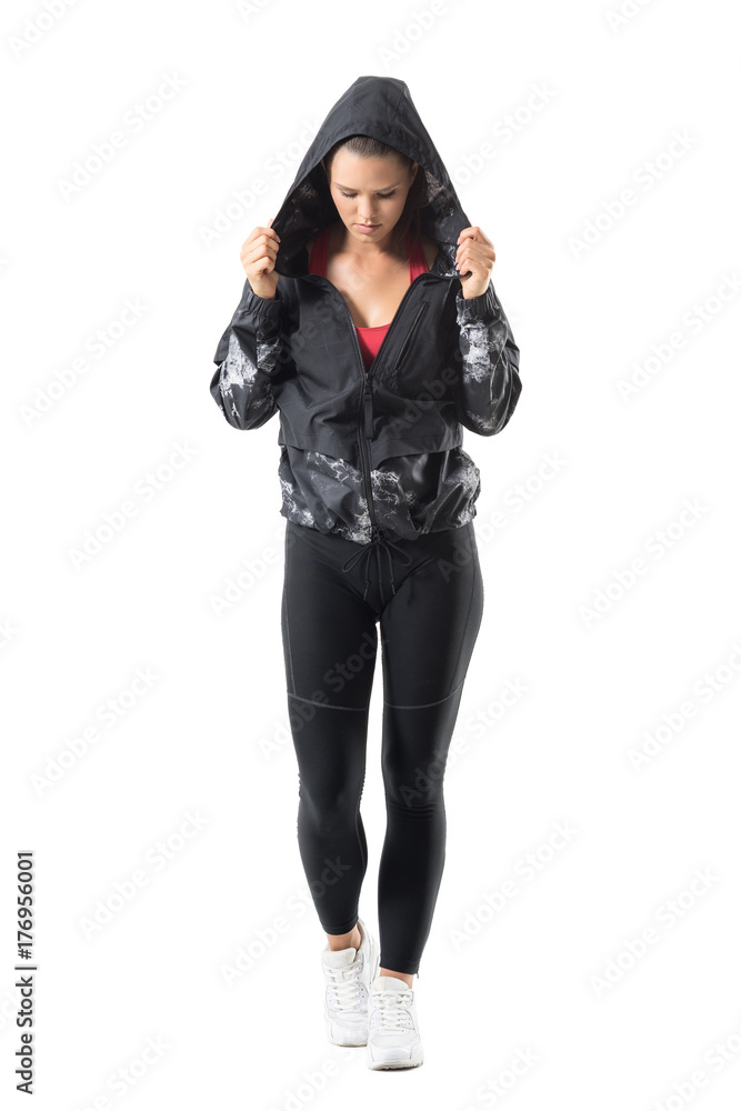 Determined young active woman holding hoodie collar looking down getting ready for running. Full body length portrait isolated on white background. Determined young active woman holding hoodie collar looking down getting ready for running. Full body length portrait isolated on white background.