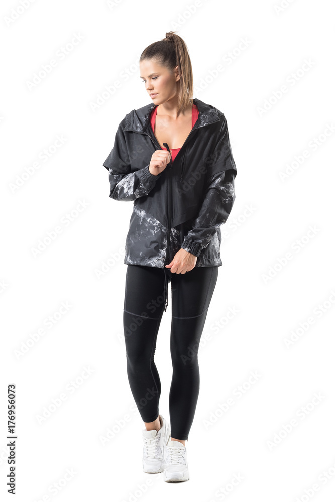Fit active woman in legging zip tracksuit jacket fastener looking down. Full body length portrait isolated on white background. Fit active woman in legging zip tracksuit jacket fastener looking down. Full body length portrait isolated on white background.