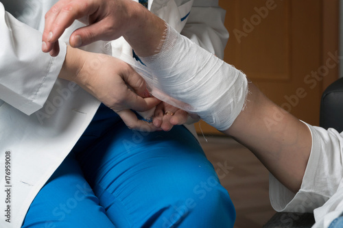 A female doctor bandages the patient's arm in his house