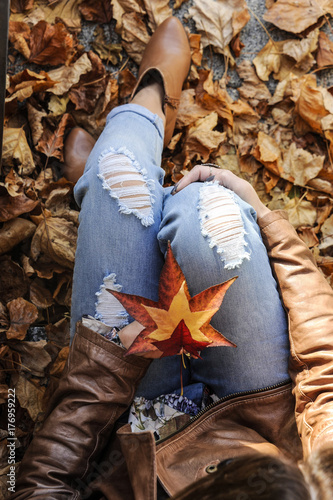 Young hipster woman is sitting among autumn leaves. Top view shot. Fashion happy life autumn concept.