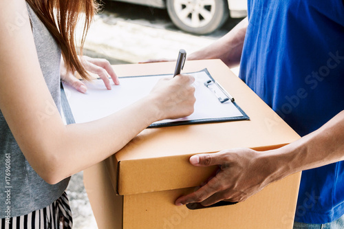 Woman putting signature in clipboard on cardboard box with delivery man © Art_Photo