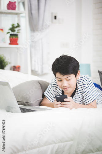Cute asian boy rest on bed and using smart cell phone.
