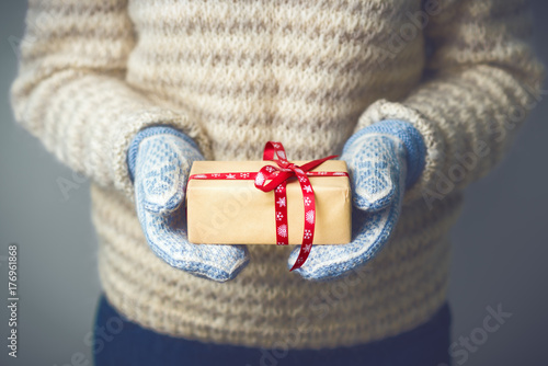 Christmas background. Girl in a warm knitted sweater and mittens is holding a Christmas present. Gifts for men. Merry Christmas. Gift for a girl. Knitted dress. Image is toned in fashionable color.