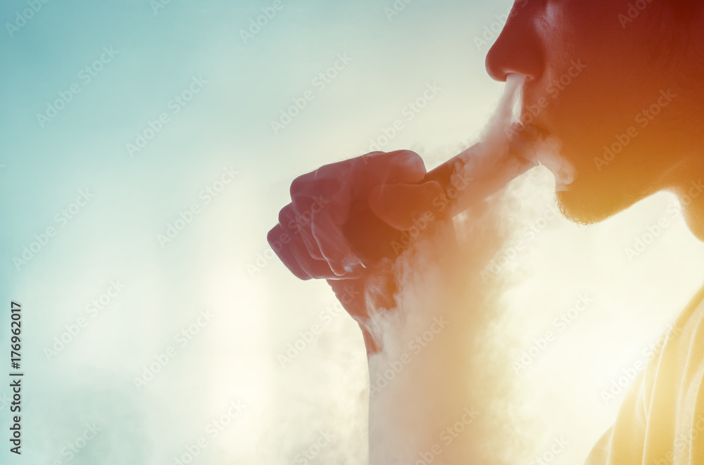Fototapeta premium Man smoke an electronic cigarette mechanical mod on the light background