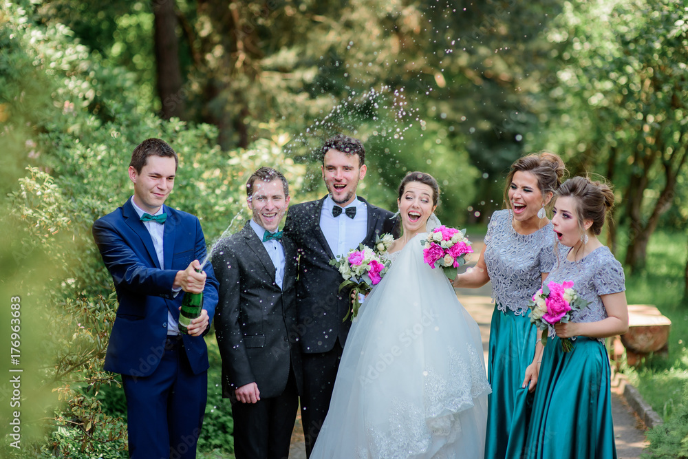 Newlyweds and friends have fun opening bottle of champagne in the park