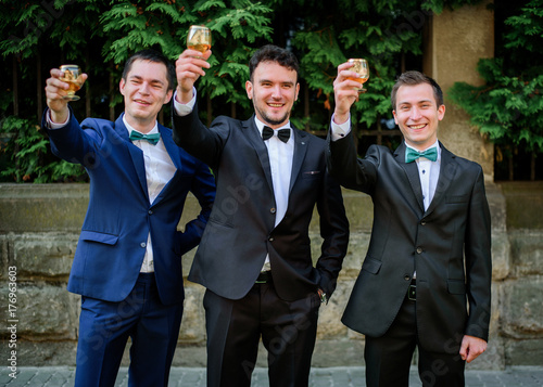 Laughing groom and groomsmen pose outside with glasses of whisky