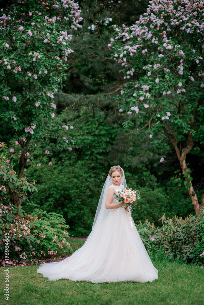 Stunning bride stands under blooming trees in the park