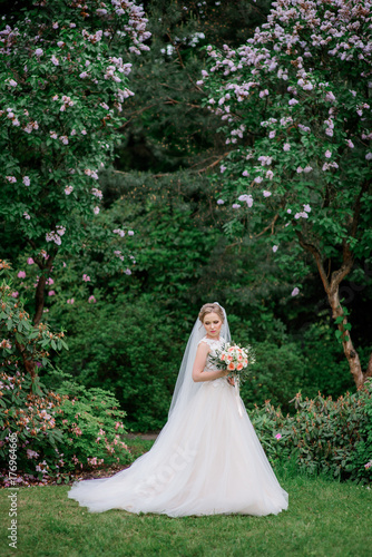 Stunning bride stands under blooming trees in the park