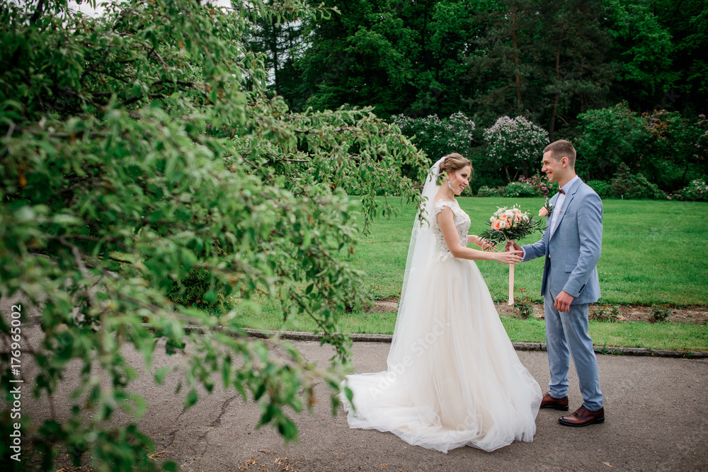 Groom gives wedding bouquet to bride while they stand in the park Groom gives wedding bouquet to bride while they stand in the park