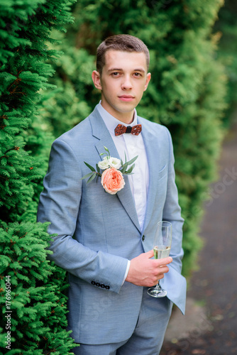 Handsome young groom in grey suit with orange boutonniere photo