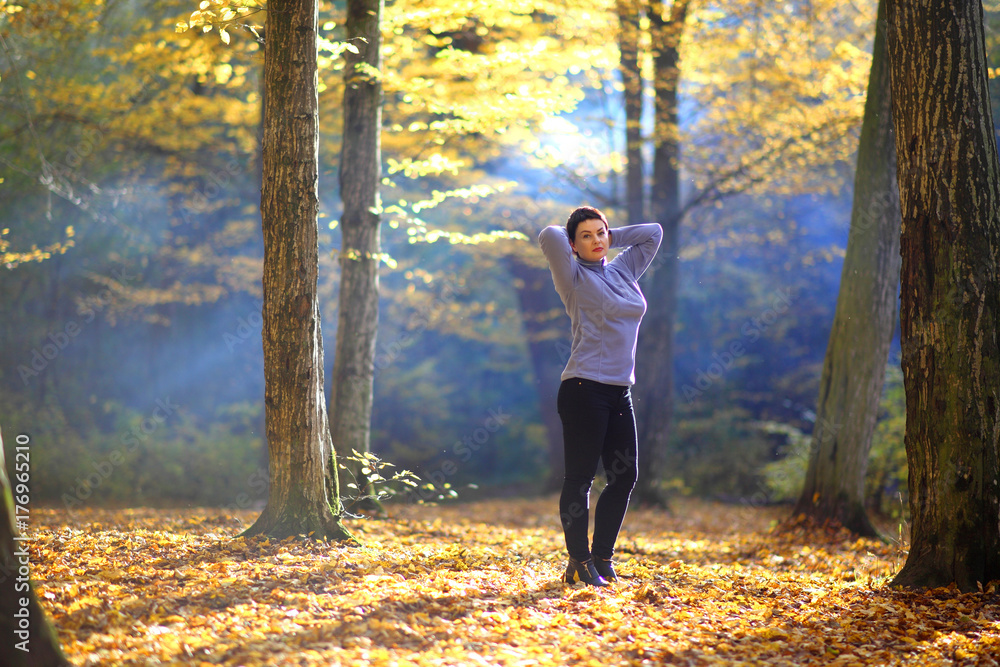 A beautiful mature woman is basking in the rays of the autumn sun in a clearing in the forest. Nice mature woman stands on a background of yellow autumn. A beautiful mature woman is basking in the rays of the autumn sun in a clearing in the forest. Nice mature woman stands on a background of yellow autumn.
