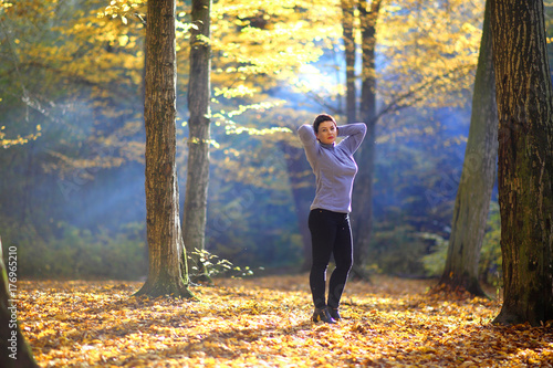 A beautiful mature woman is basking in the rays of the autumn sun in a clearing in the forest. Nice mature woman stands on a background of yellow autumn. 