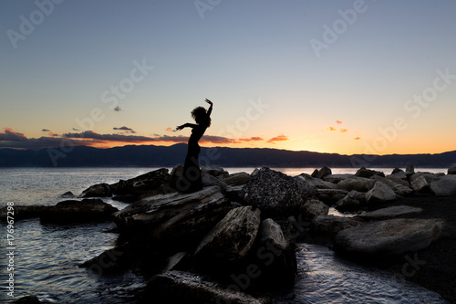ragazza in silhouette danza sugli scogli al tramonto in riva al mare