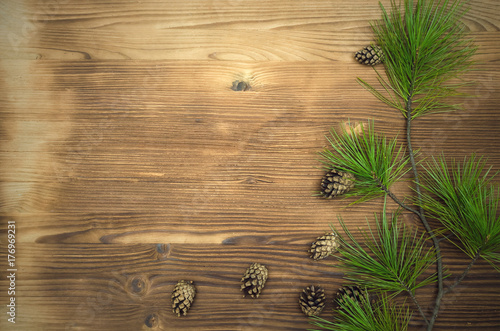 Fir tree branches with scattered cones around on brown wooden table surface background with copy space. Christmas table decoration.