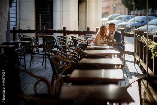 Dreamy newlyweds sit in an empty street cafe